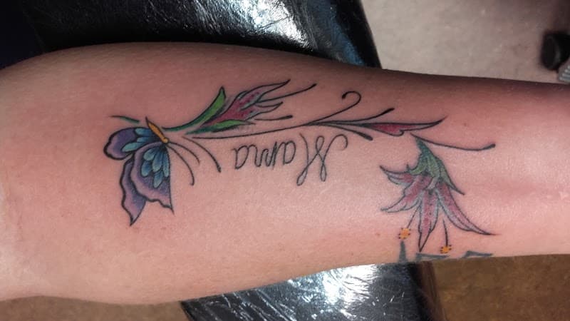 Kleurrijke vlinder en bloemen met 'Mama' tekst op onderarm.
