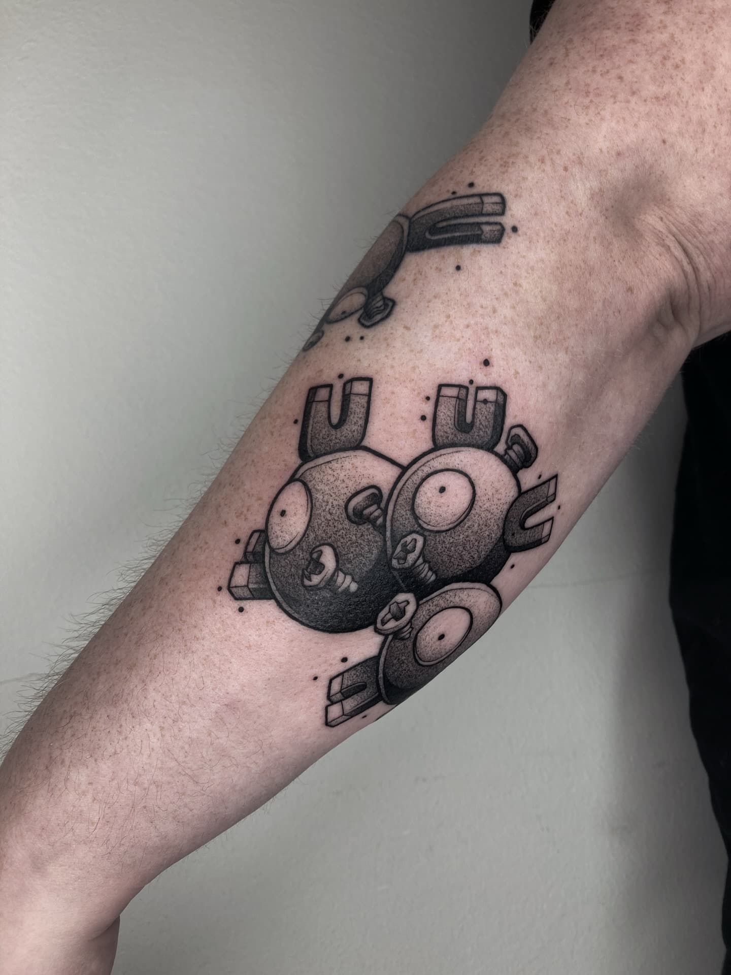 Zwart-wit Pokémon tattoo van Magnemite en Magneton op bovenarm.