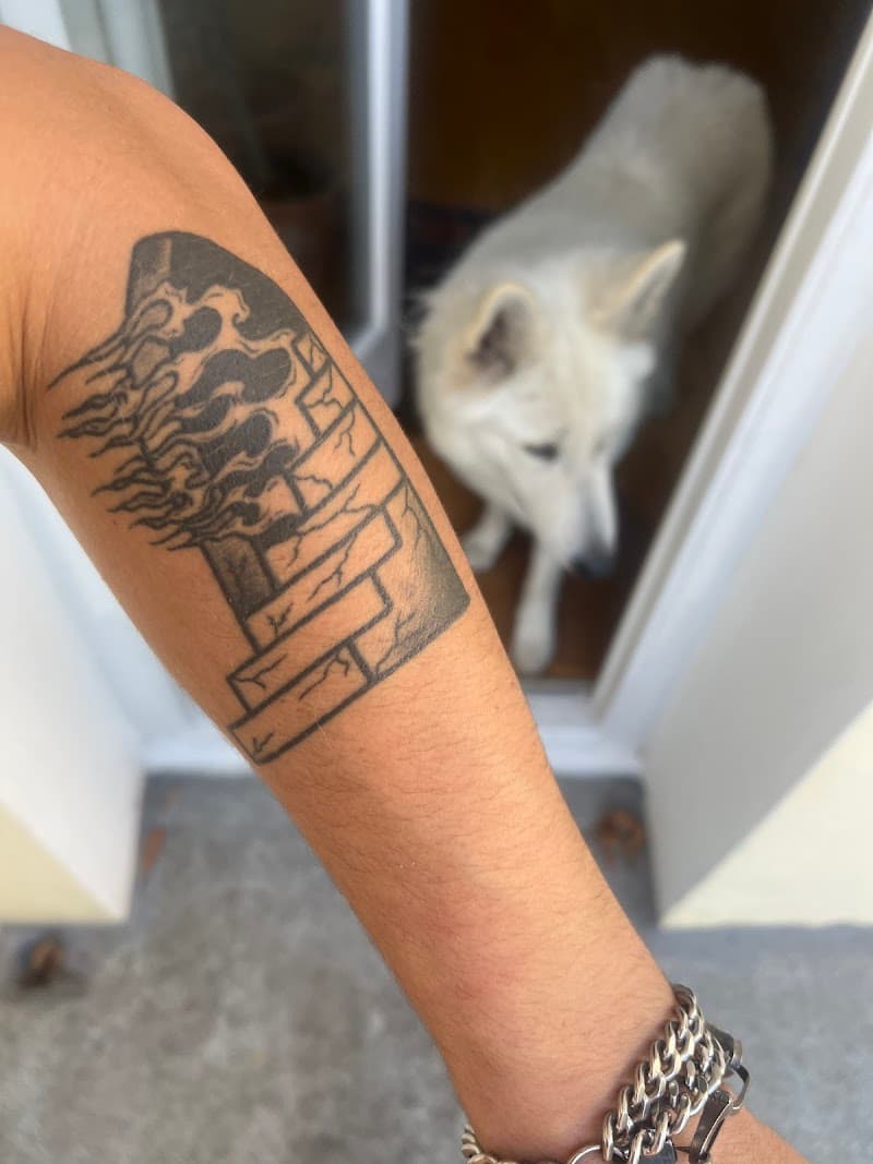 Zwart-wit tattoo van een stenen trap die overgaat in vlammen op de onderarm.