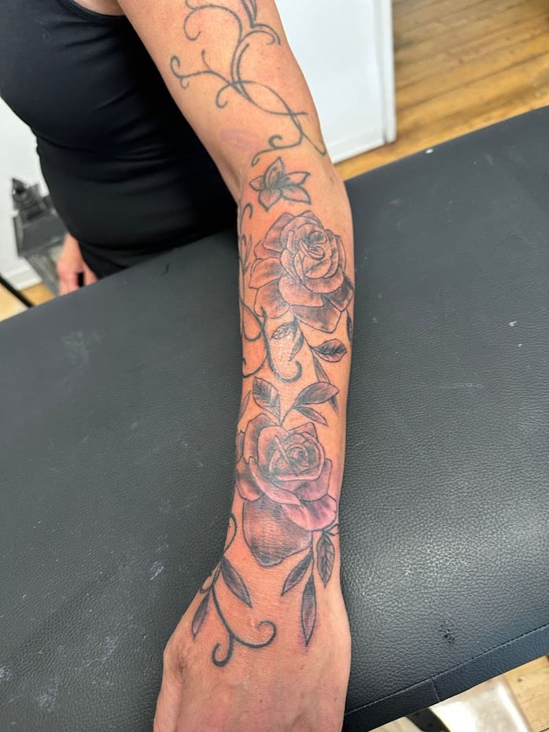 Zwart-grijze rozen en ranken tattoo op onderarm en hand.