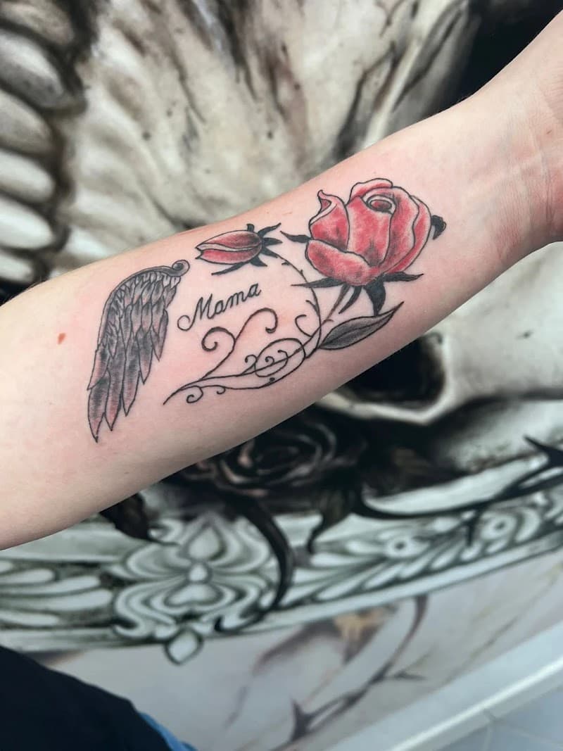 Rode roos, vleugel en 'Mama' tekst tattoo op onderarm.