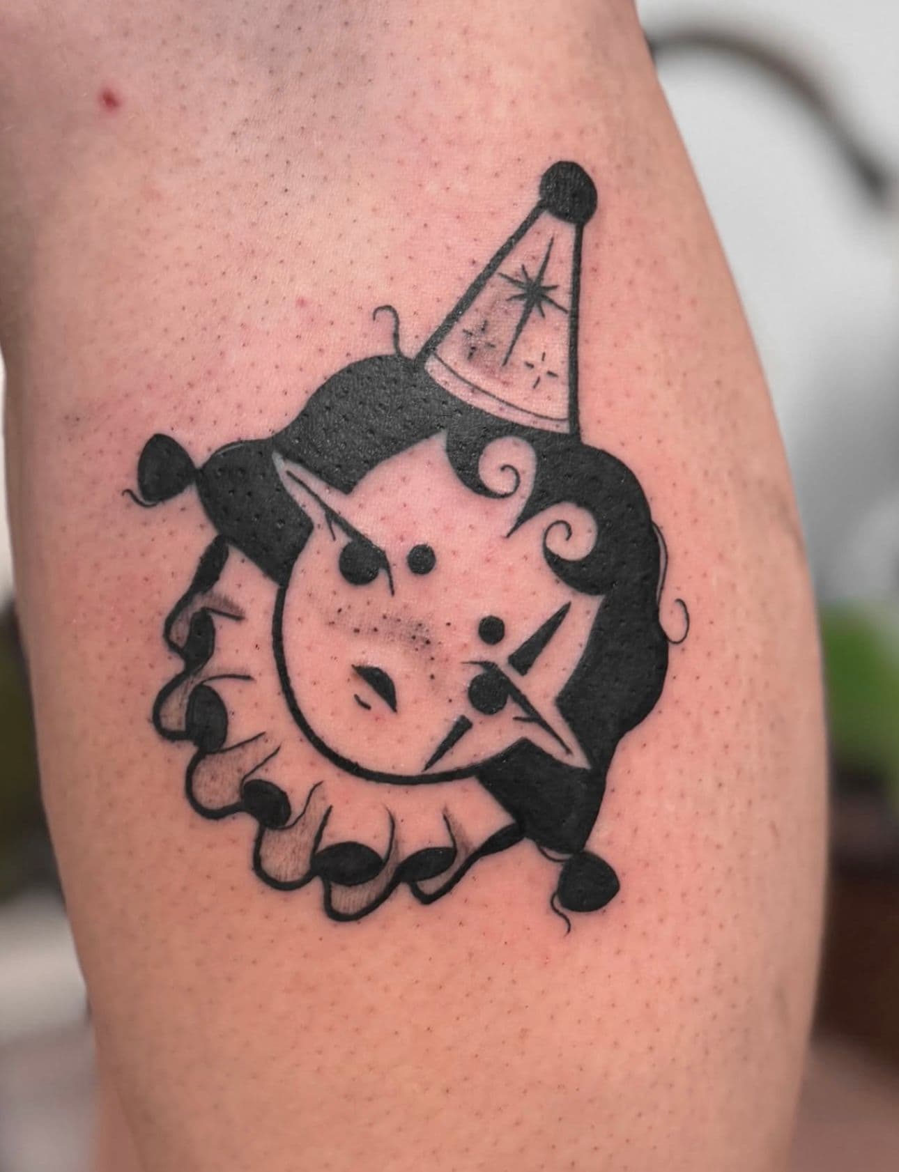 Kleine blackwork tattoo van een clown of pierrot hoofd met een feesthoedje.