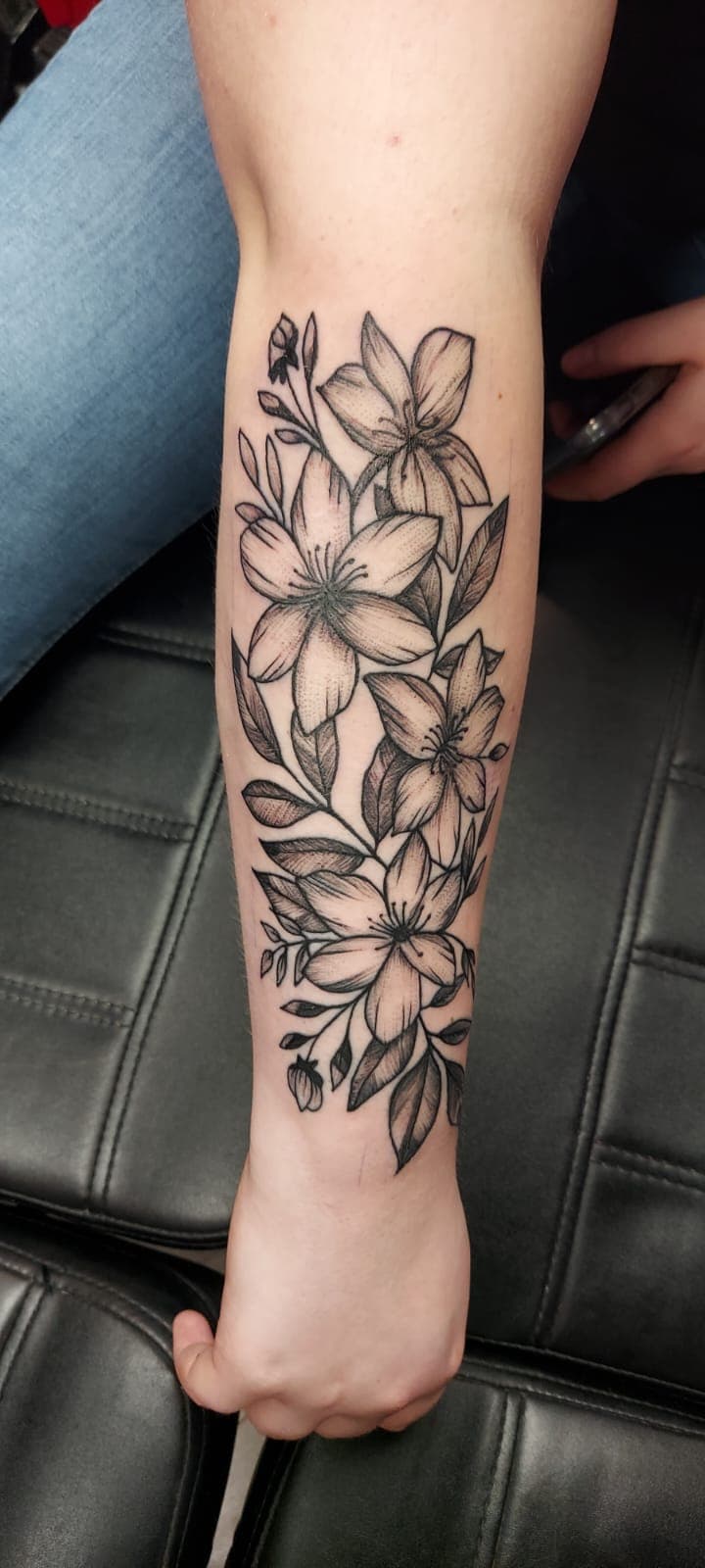 Fineline bloemen tattoo met lelies op onderarm.