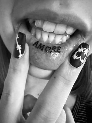 Zwart-wit foto van 'AMORE' tattoo aan de binnenkant van de onderlip.