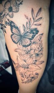 Vlinder en lelies in fineline en dotwork op het bovenbeen.