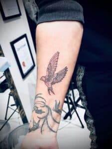 Fineline vogel tattoo en abstract patroon op onderarm.