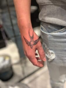 Zwart-wit zwaluw tattoo op de bovenkant van de hand.