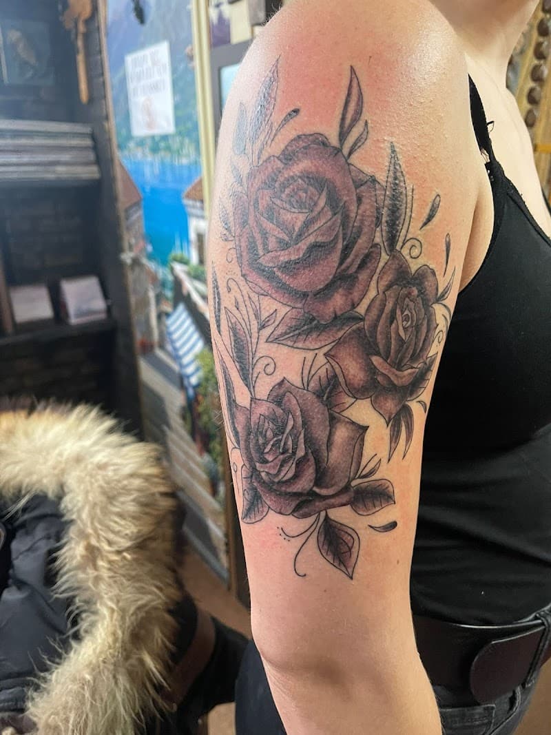 Zwart-wit tattoo van drie rozen met bladeren op de bovenarm.