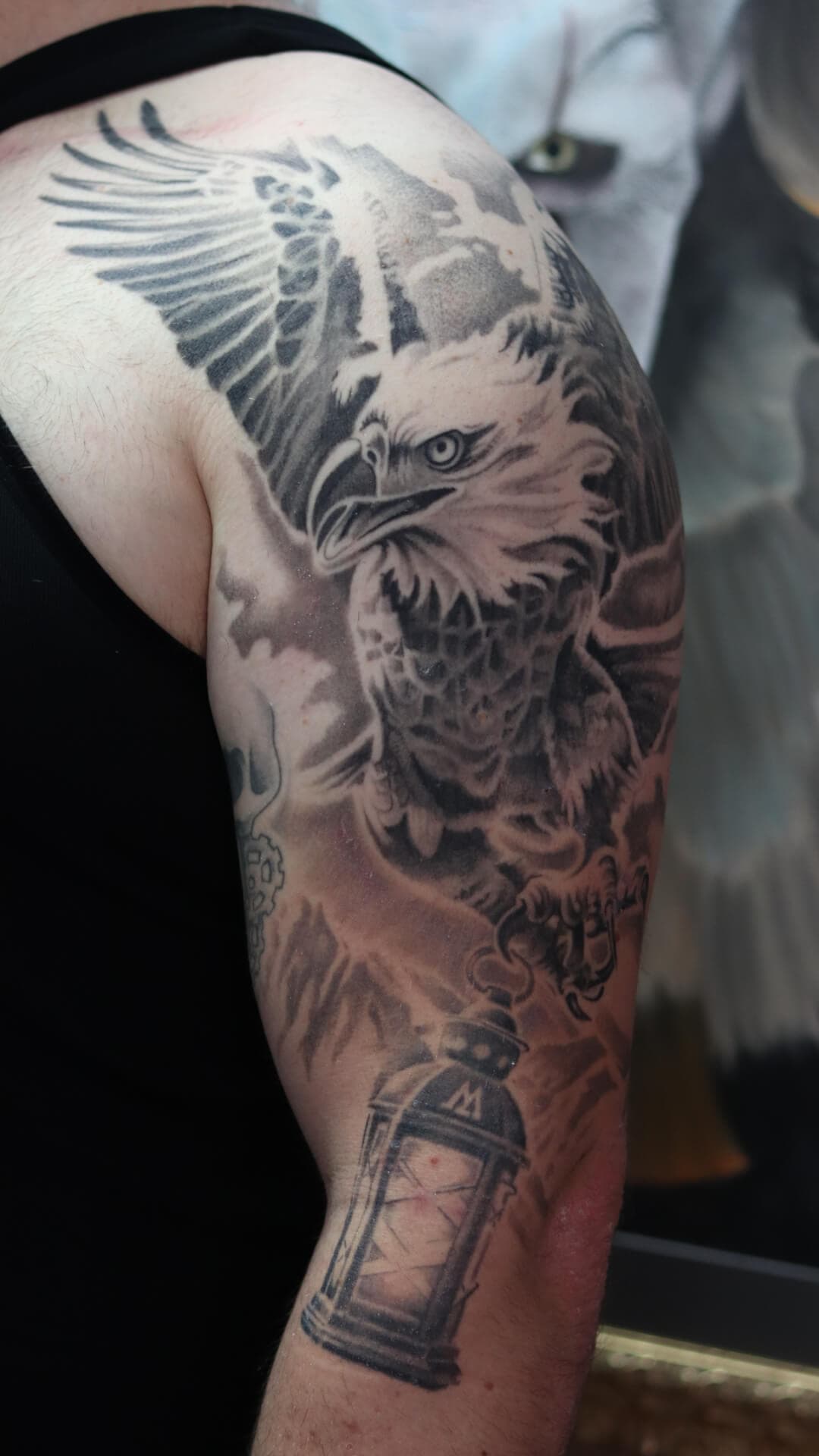 Zwart-wit tattoo van een adelaar die een lantaarn vasthoudt op de bovenarm.