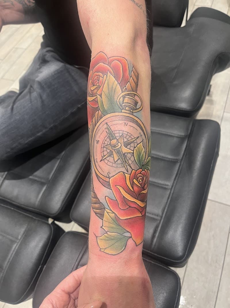 Neo-traditional tattoo van een kompas met rode rozen op de onderarm.