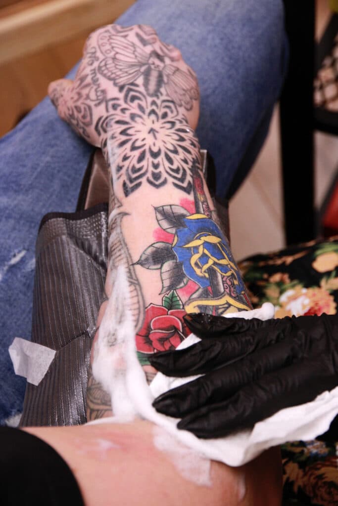 Close-up van traditionele roos en dolk tattoo op onderarm, en mandala op hand.