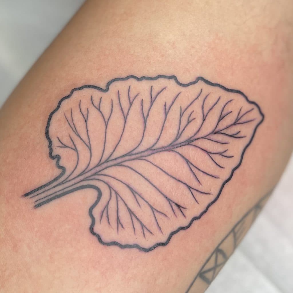 Minimalistische lijnwerk tattoo van een blad op het been.