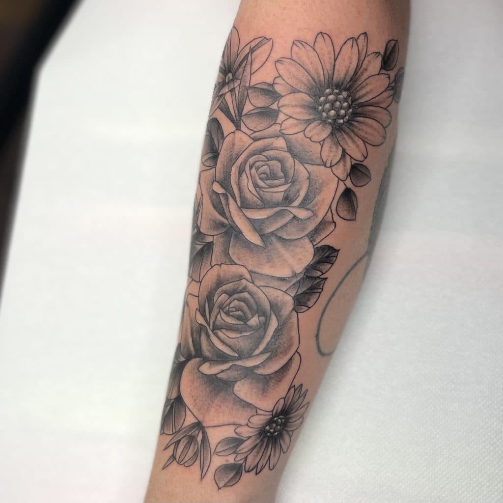 Illustratieve bloemen tattoo met rozen en madeliefjes op onderarm.