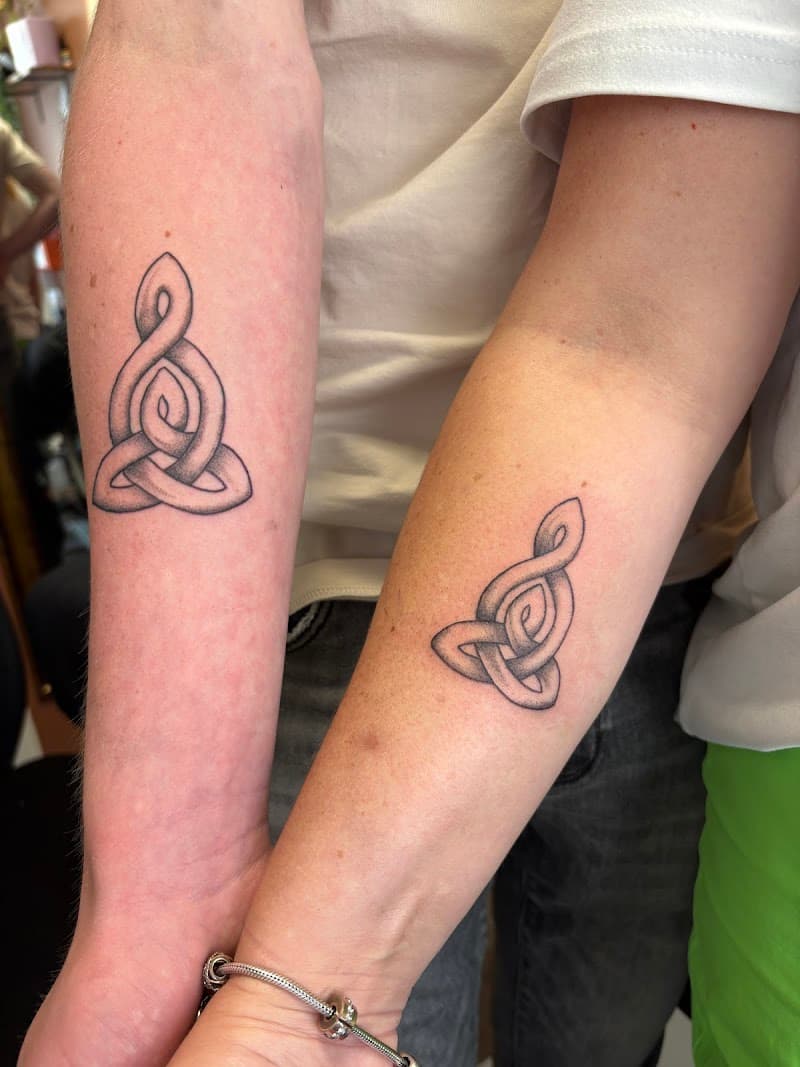 Twee bijpassende Keltische moeder-kind knoop tattoos op onderarmen.