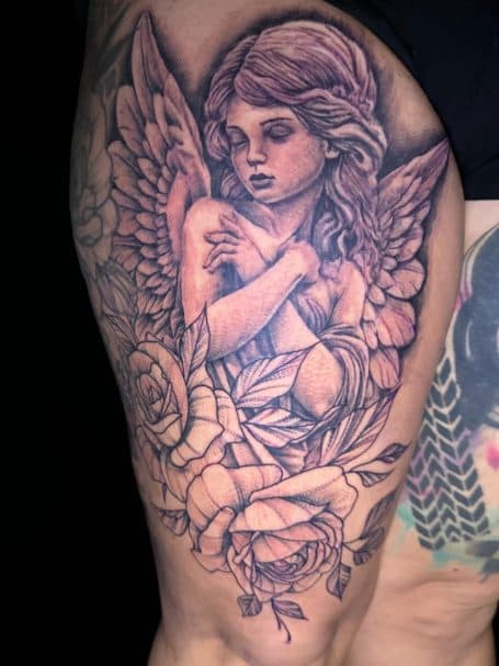 Zwart-wit tattoo van een engel met vleugels en rozen op het bovenbeen.