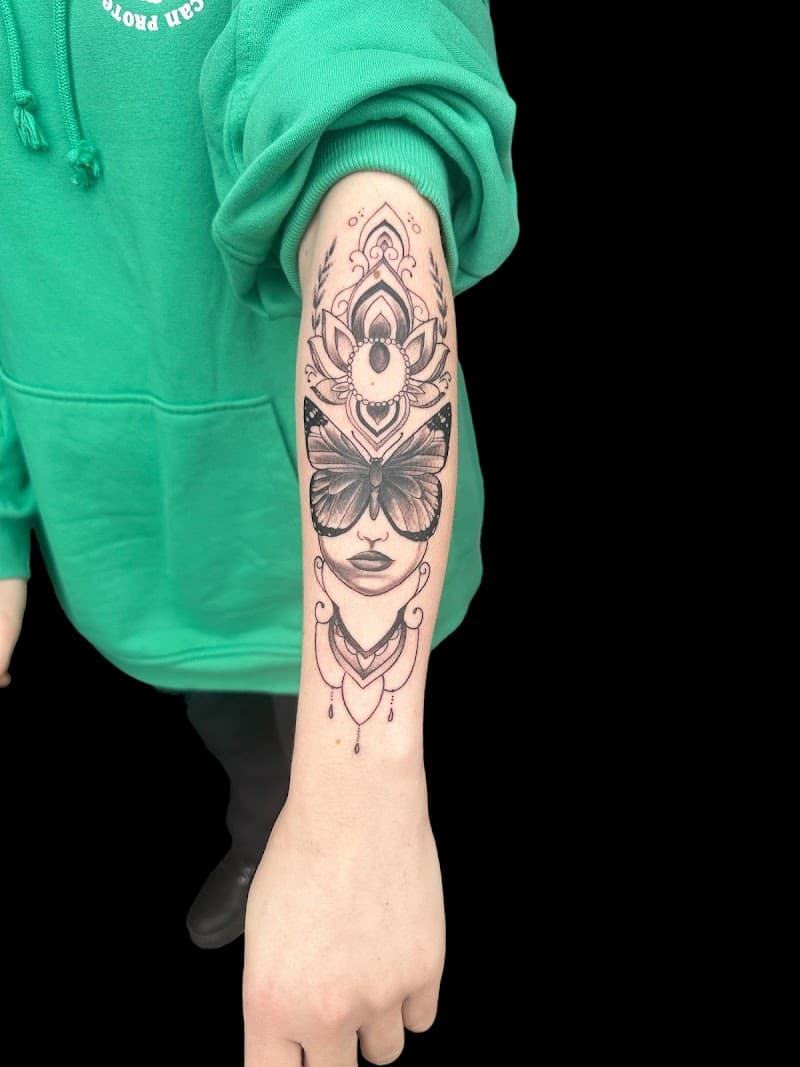 Zwart-wit tattoo van een vrouwengezicht met een vlinder voor de ogen en mandala.