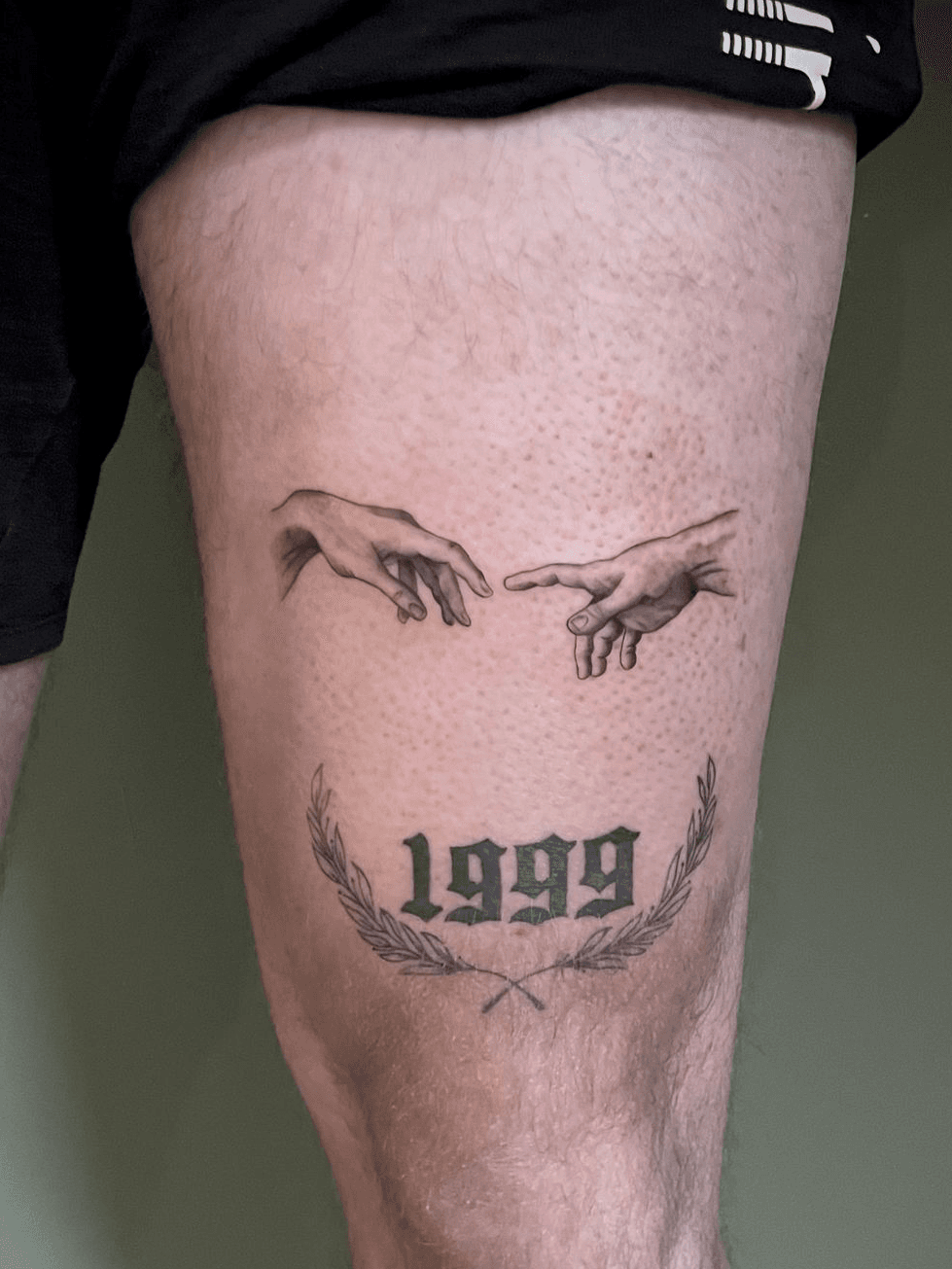 Creatie van Adam handen en 1999 met lauwerkrans op bovenbeen.