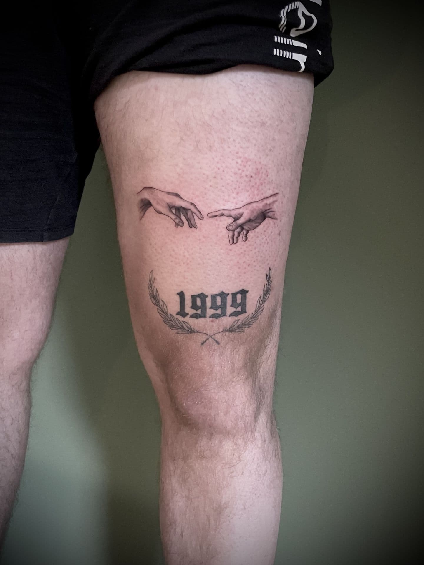 Fineline handen van Adam en 1999 met lauwerkrans op bovenbeen.