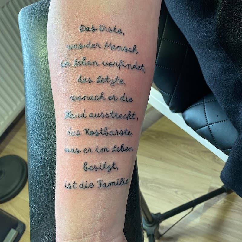 Duitse tekst tattoo over familie op onderarm in sierlijk handschrift.