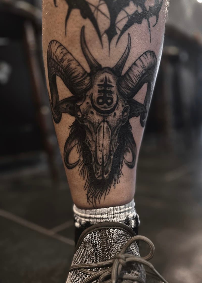 Zwart-wit tattoo van een ramschedel met een Leviathan kruis op het voorhoofd.