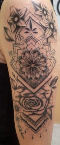 Zwart-wit mandala en bloemen half-sleeve tattoo op bovenarm.