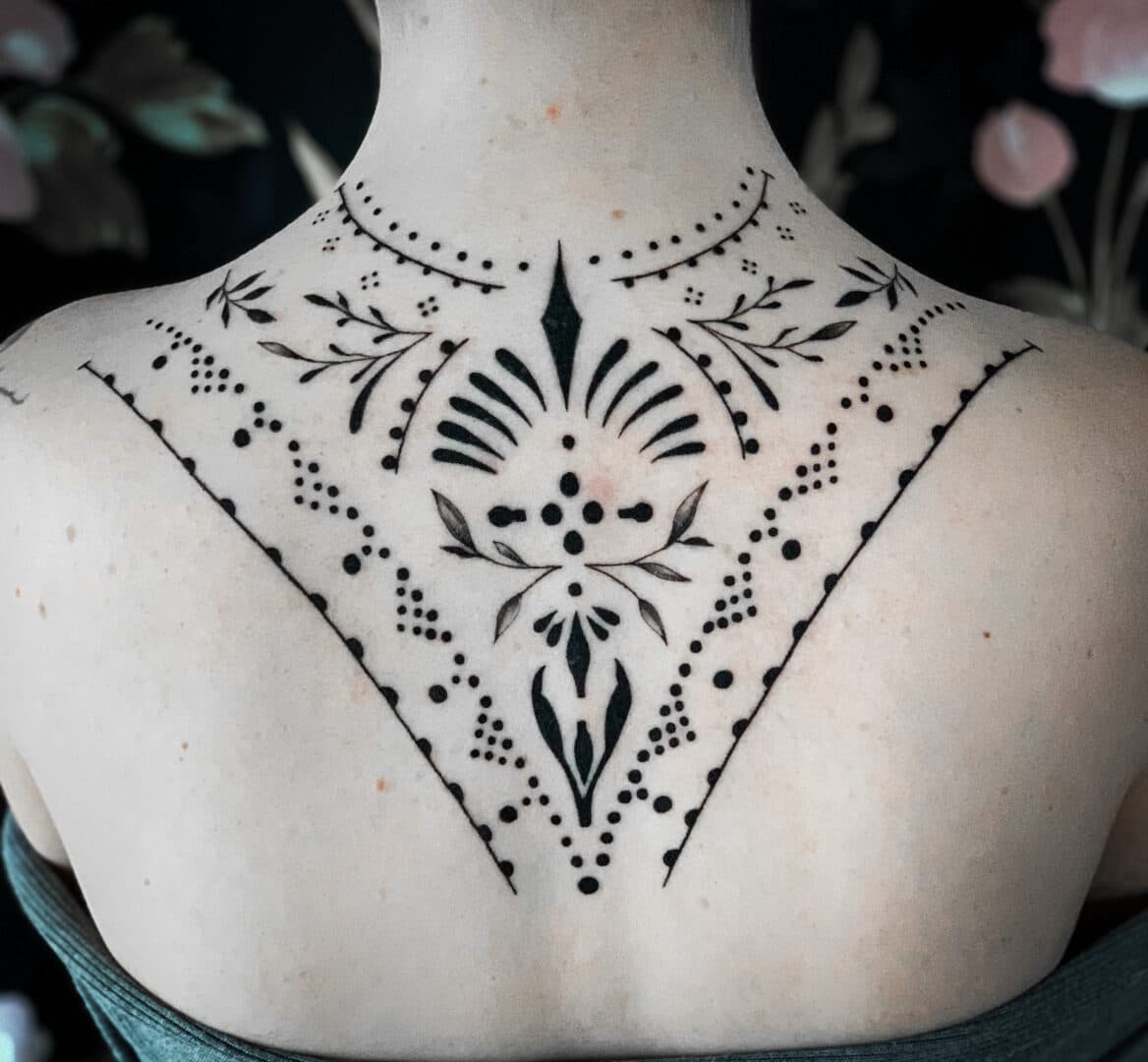 Sierlijke ornamentele tattoo met dotwork en lijnwerk op de bovenrug.