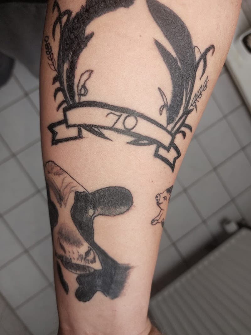 Illustratieve tattoos van een krans met '70', een koe en een varken op de onderarm.