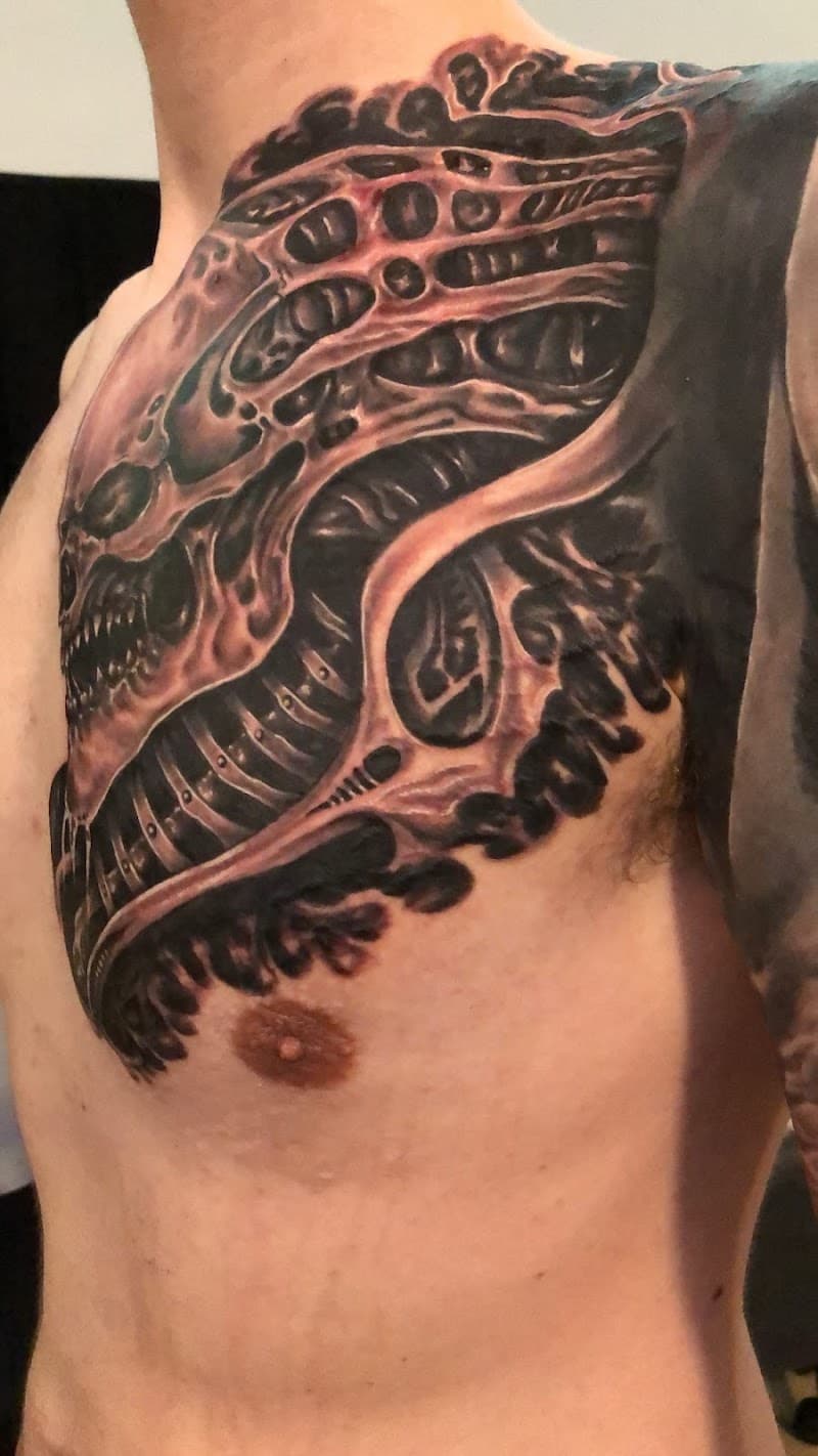 Grote biomechanische tattoo op borst en schouder.