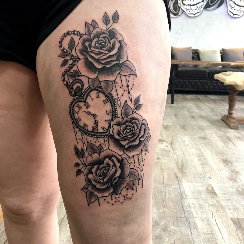 Zwart-wit tattoo van een hartvormig zakhorloge met rozen en parels op het bovenbeen.