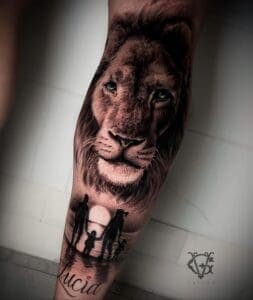 Realistische leeuw met familie silhouet en naam 'Lucia' op onderbeen.