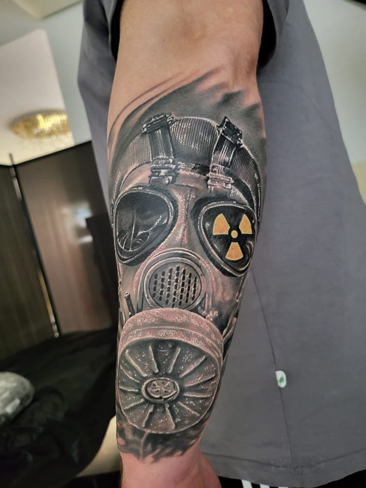 Realistische gasmasker tattoo met geel radioactief symbool op onderarm.