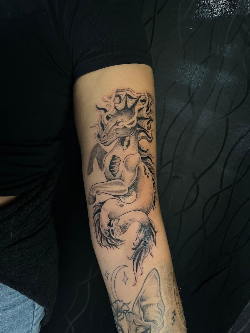 Zwart-wit tattoo van een mythisch zeepaard/draak wezen op de bovenarm.