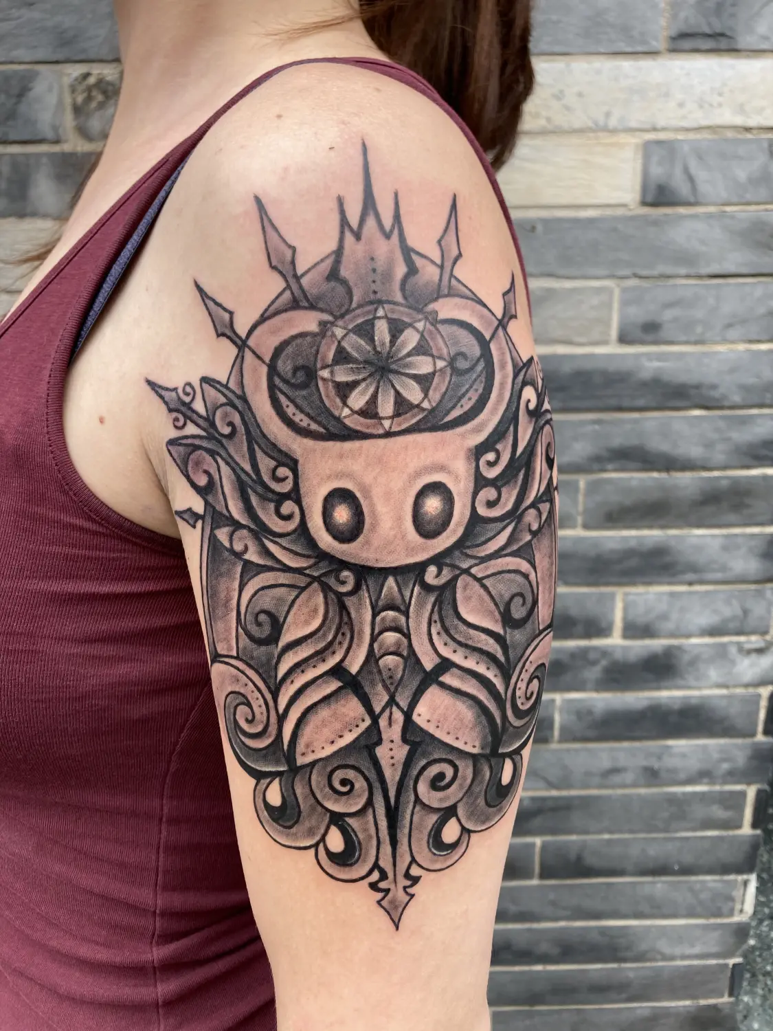 Zwart-wit Hollow Knight tattoo met ornamenten op bovenarm