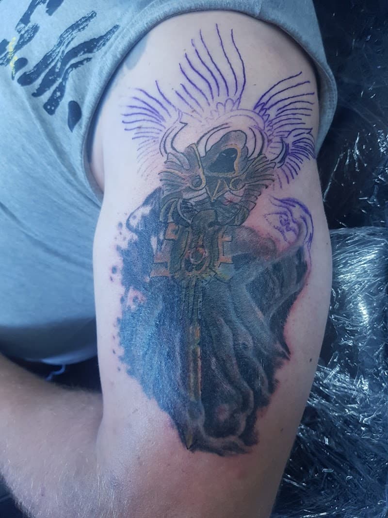 Duistere getatoeëerde gedaante met kap, vleugels (stencil) en zwaard op bovenarm.