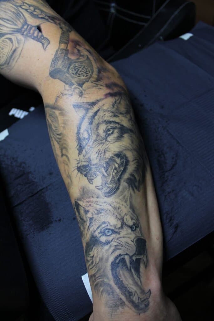 Twee grommende wolven en een hamer (Mjölnir) op een onderbeen.