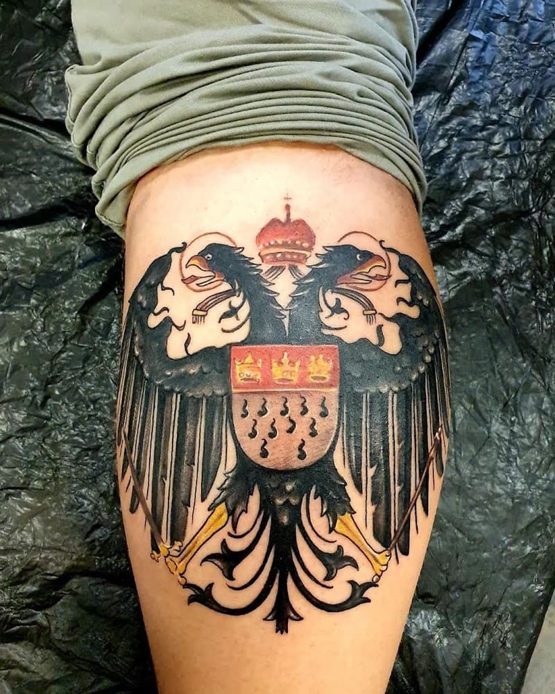 Grote, gekleurde tattoo van een dubbele adelaar met kroon en wapenschild op het bovenbeen.