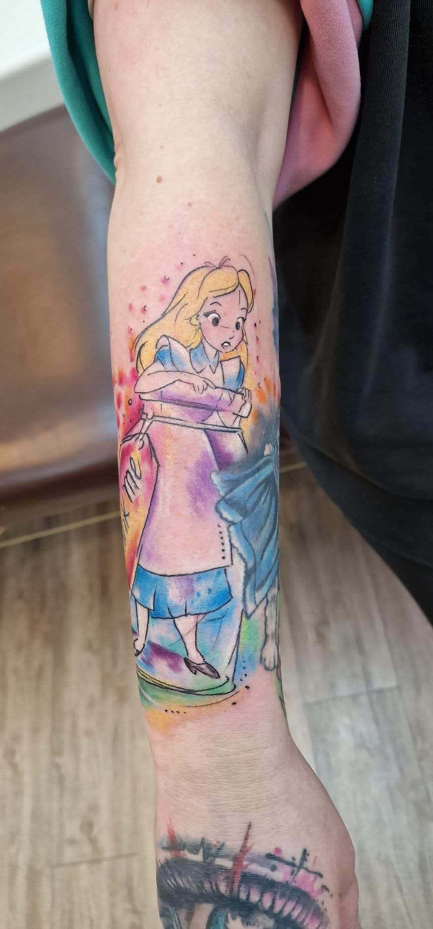 Watercolor tattoo van Alice in Wonderland in een fles op de onderarm.