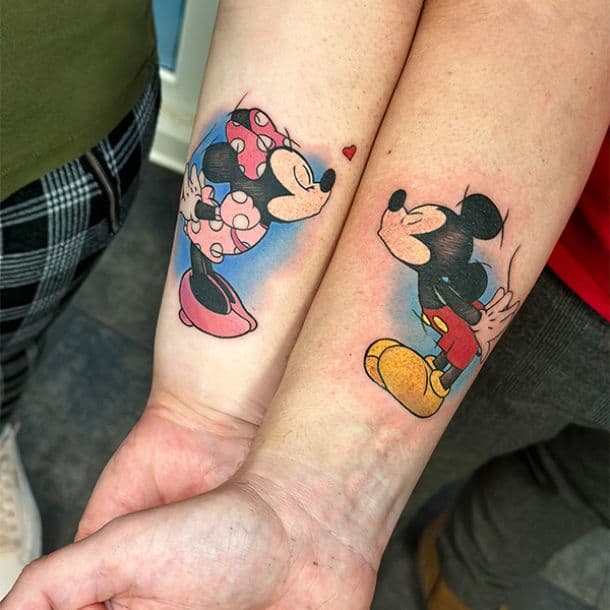 Kleurrijke Mickey en Minnie Mouse koppel tattoos op onderarmen.