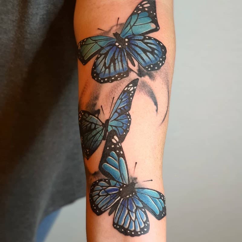 Drie blauwe monarchvlinders in realistische stijl op de onderarm.