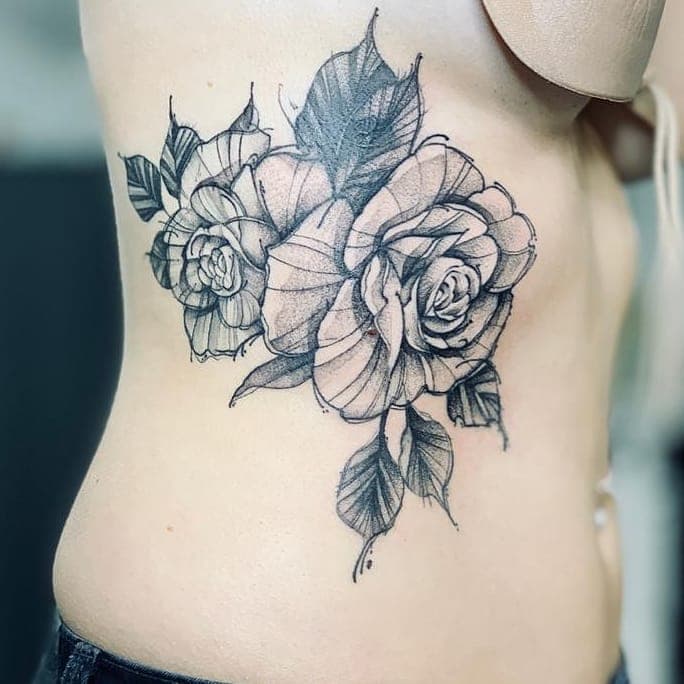 Schetsmatige rozen tattoo op de ribben in zwart-wit.