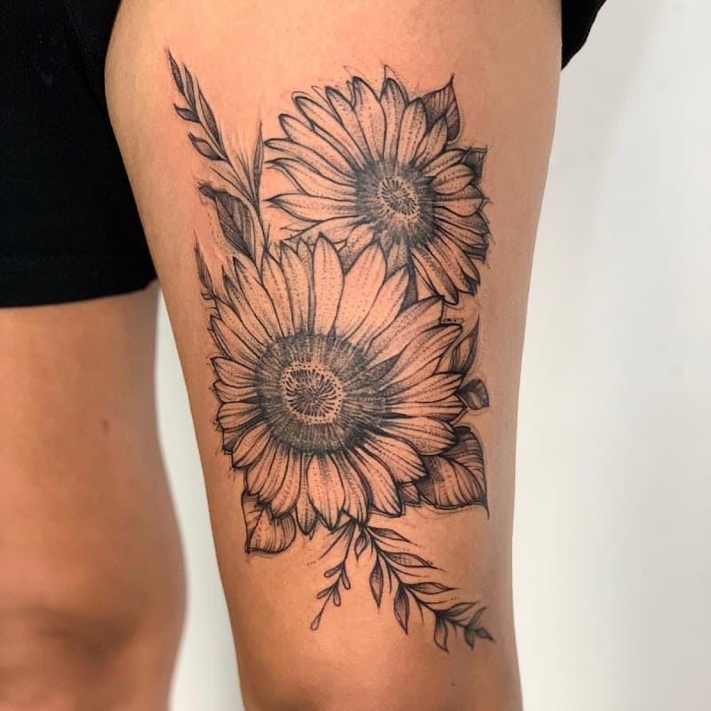 Twee zonnebloemen met bladeren in blackwork stijl op het bovenbeen.