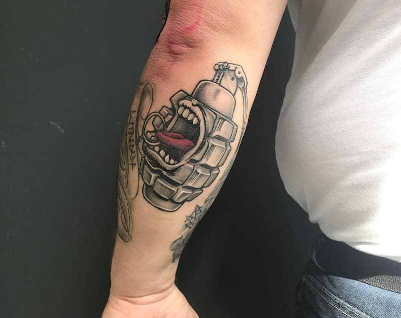 Zwart-grijze handgranaat met een schreeuwend gezicht en rode tong op de onderarm.