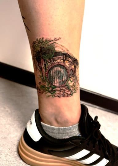 Gedetailleerde Hobbit-huis (Bag End) tattoo op de enkel.