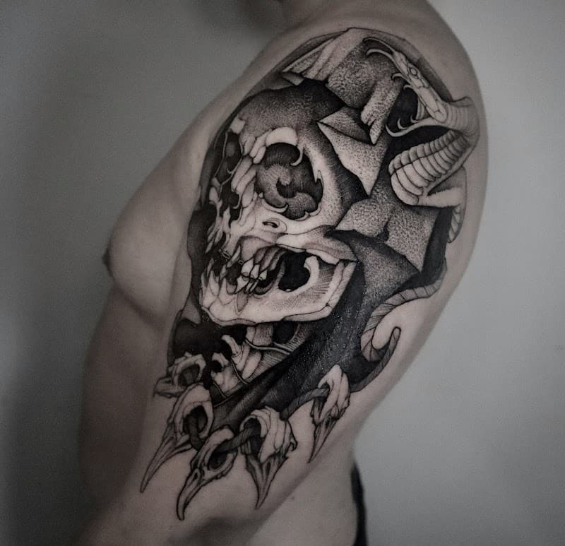 Blackwork tattoo van een schedel, slang en klauwen op de bovenarm.