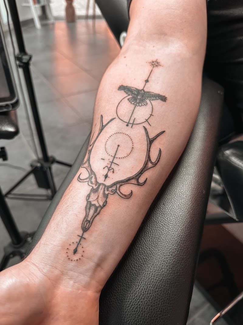 Fineline tattoo van een hertenschedel met gewei, een vogel en geometrische lijnen.