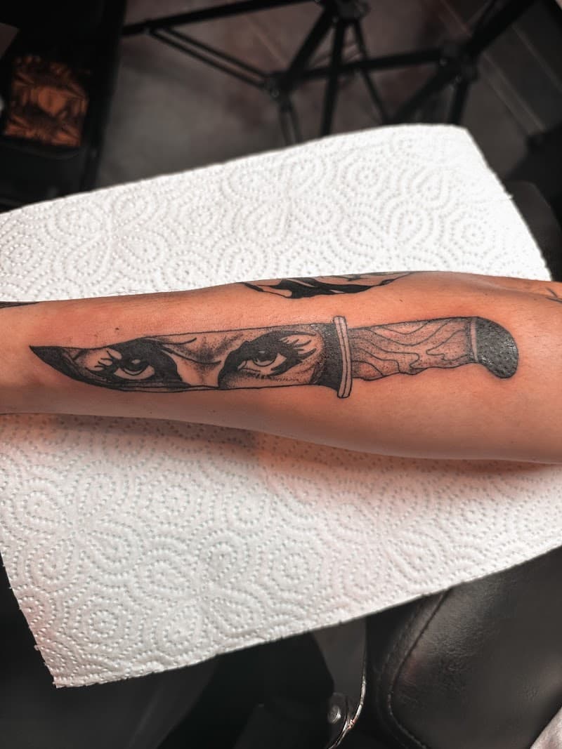 Zwart-wit tattoo van een mes met vrouwenogen op het lemmet.
