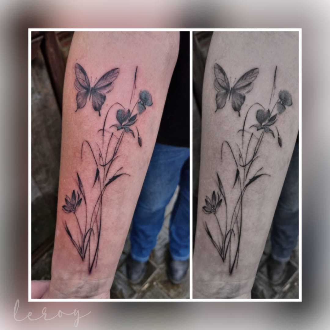 Zwart-wit fineline tattoo van een vlinder en bloemen op de onderarm.
