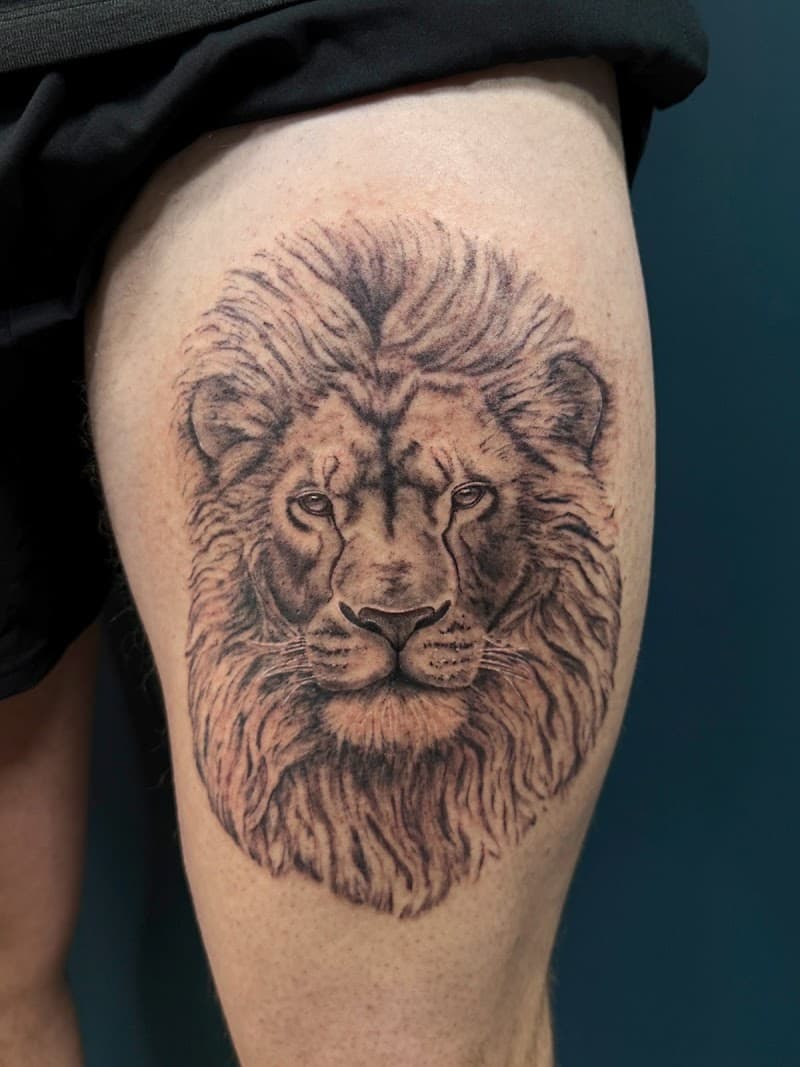 Realistische leeuwenkop tattoo op bovenbeen.