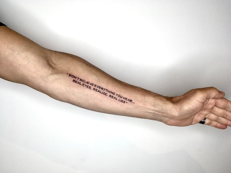 Tekst tattoo met de quote 'DON'T BELIEVE EVERYTHING YOU HEAR...' op de onderarm.