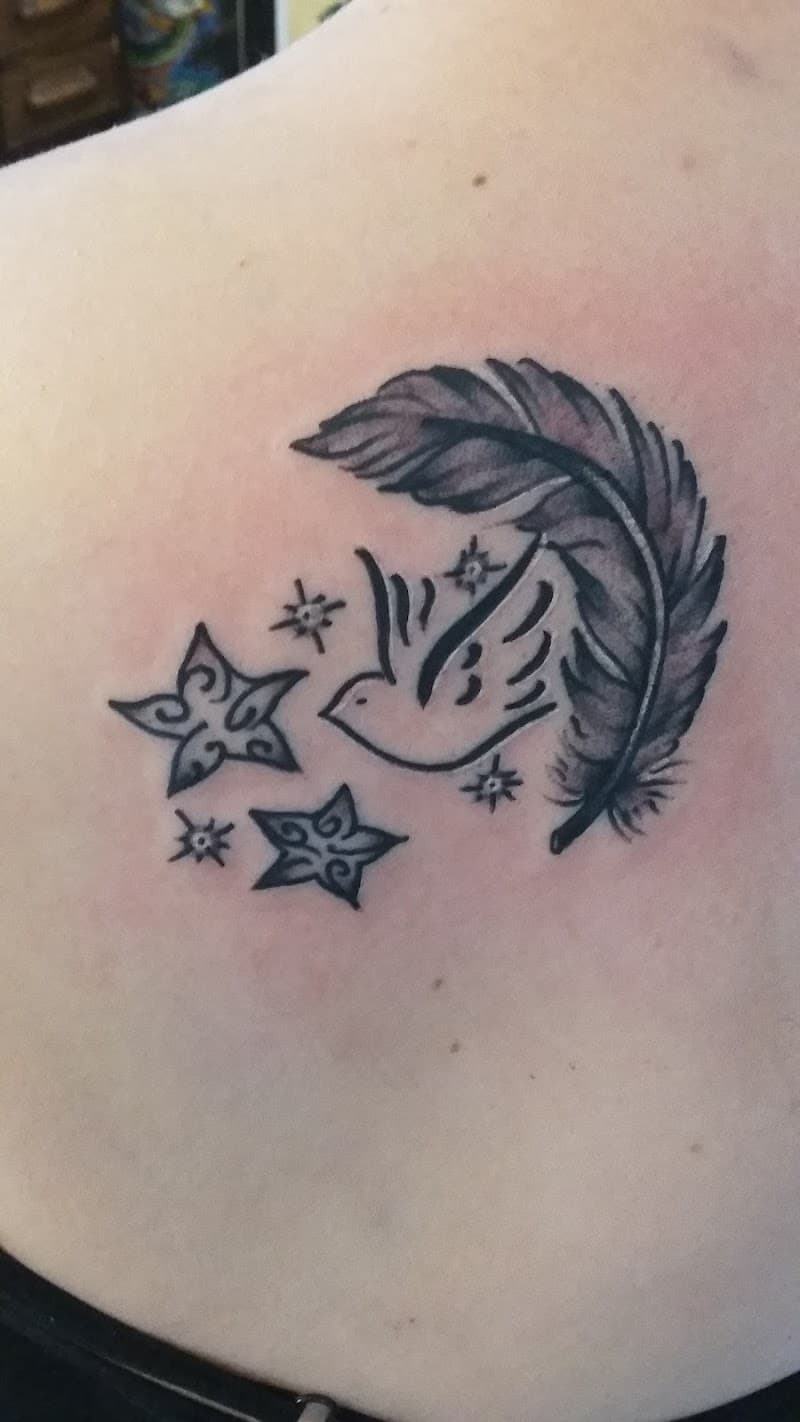 Blackwork tattoo van een veer, gestileerde vogel en sterren op de schouder.